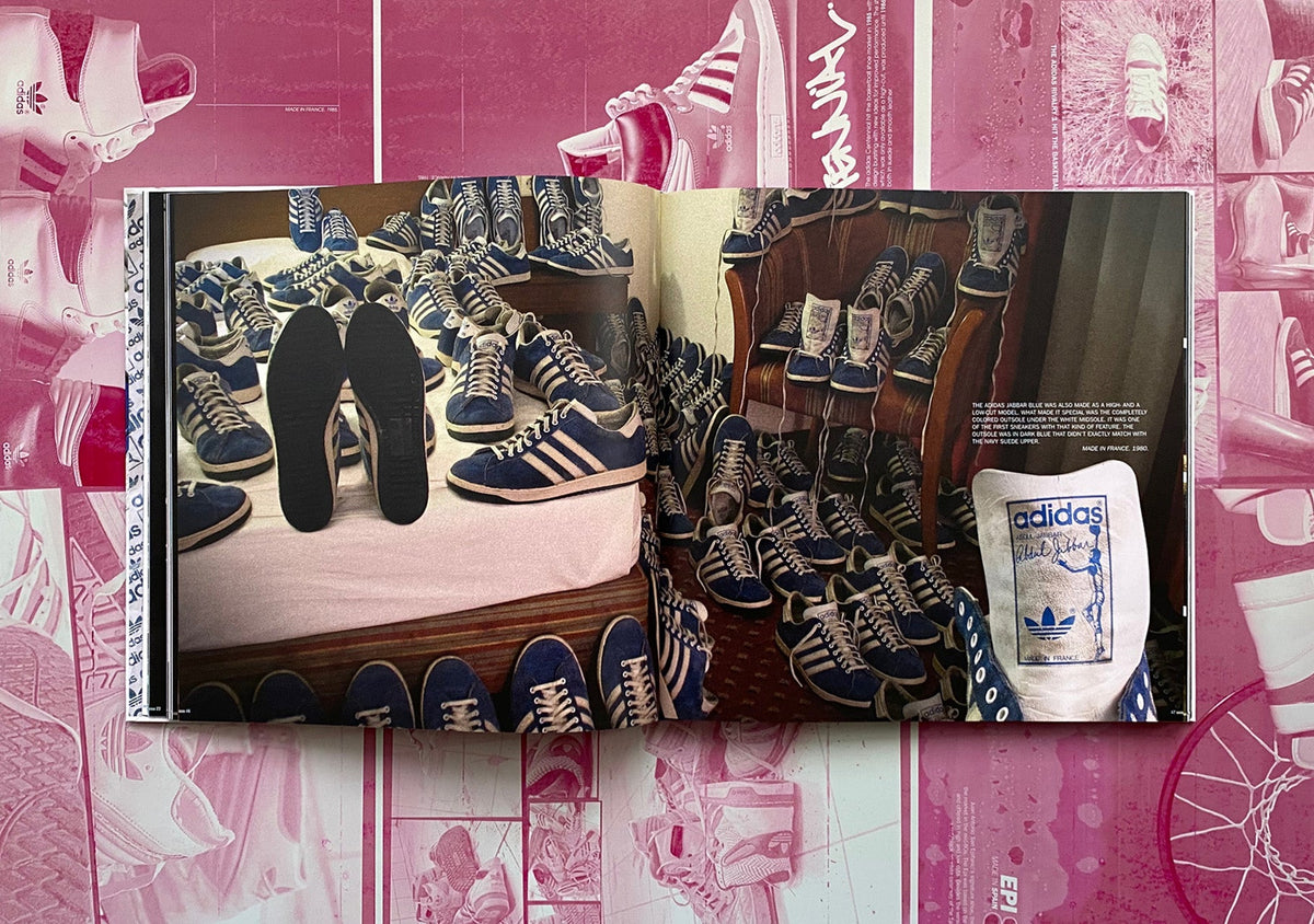 Aufgeschlagenes Buch zeigt Fotos von blauen Adidas-Sneakern und einem Beutel vor pinkem Hintergrund.