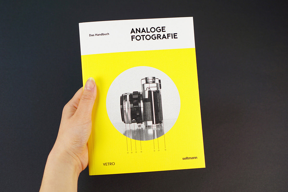 Eine Hand hält das gelbe Buch Analoge Fotografie mit einer Kameraabbildung auf dem Cover.
