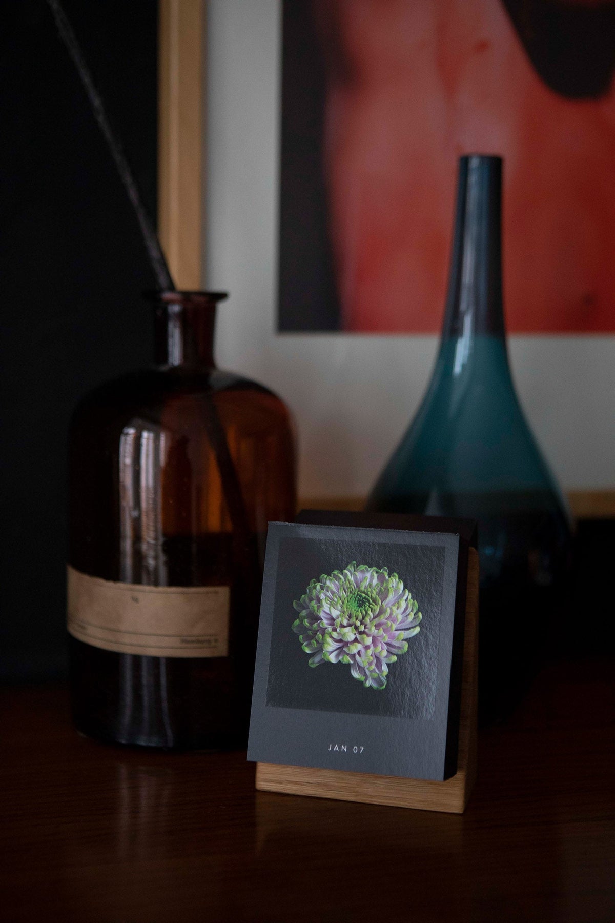 Tischkalender Flamboyant Flowers mit lila Blüte und Datum JAN 07 auf Holzsockel vor Glasflaschen
