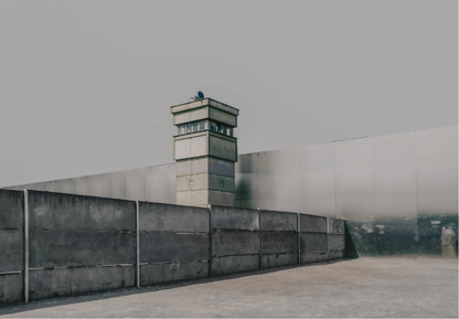 Betonmauer mit Wachturm vor grauem Himmel