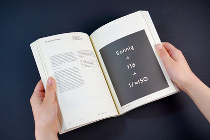 Aufgeschlagenes Buch mit den Händen gehalten, zeigt auf der rechten Seite eine Belichtungsformel auf schwarzem Grund.