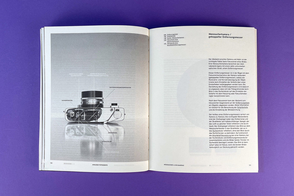 Aufgeschlagenes Buch mit einer schematischen Zeichnung einer Spiegelreflexkamera und begleitendem Text auf violettem Untergrund.