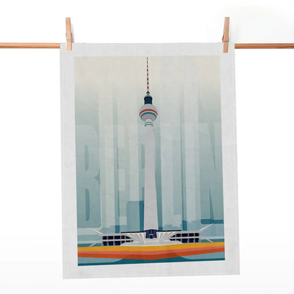 Helles Geschirrtuch mit grafischem Motiv des Berliner Fernsehturms und Schriftzug BERLIN, an einer Holzstange aufgehängt.