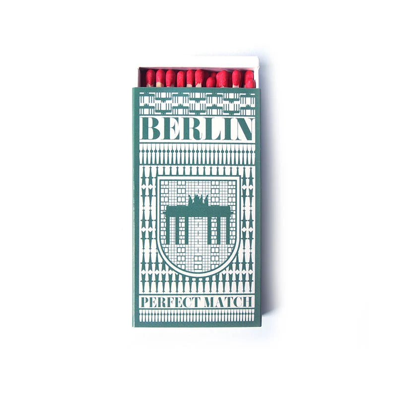 Grüne Streichholzschachtel mit Berlin-Schriftzug und Brandenburger Tor Motiv, geöffnet mit roten Zündhölzern.