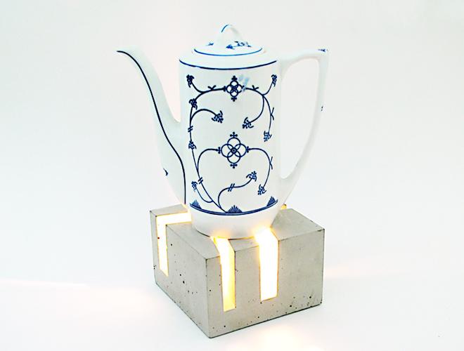 Weiße Teekanne mit Blauornament auf beleuchtetem Beton-Stövchen im Würfelformat