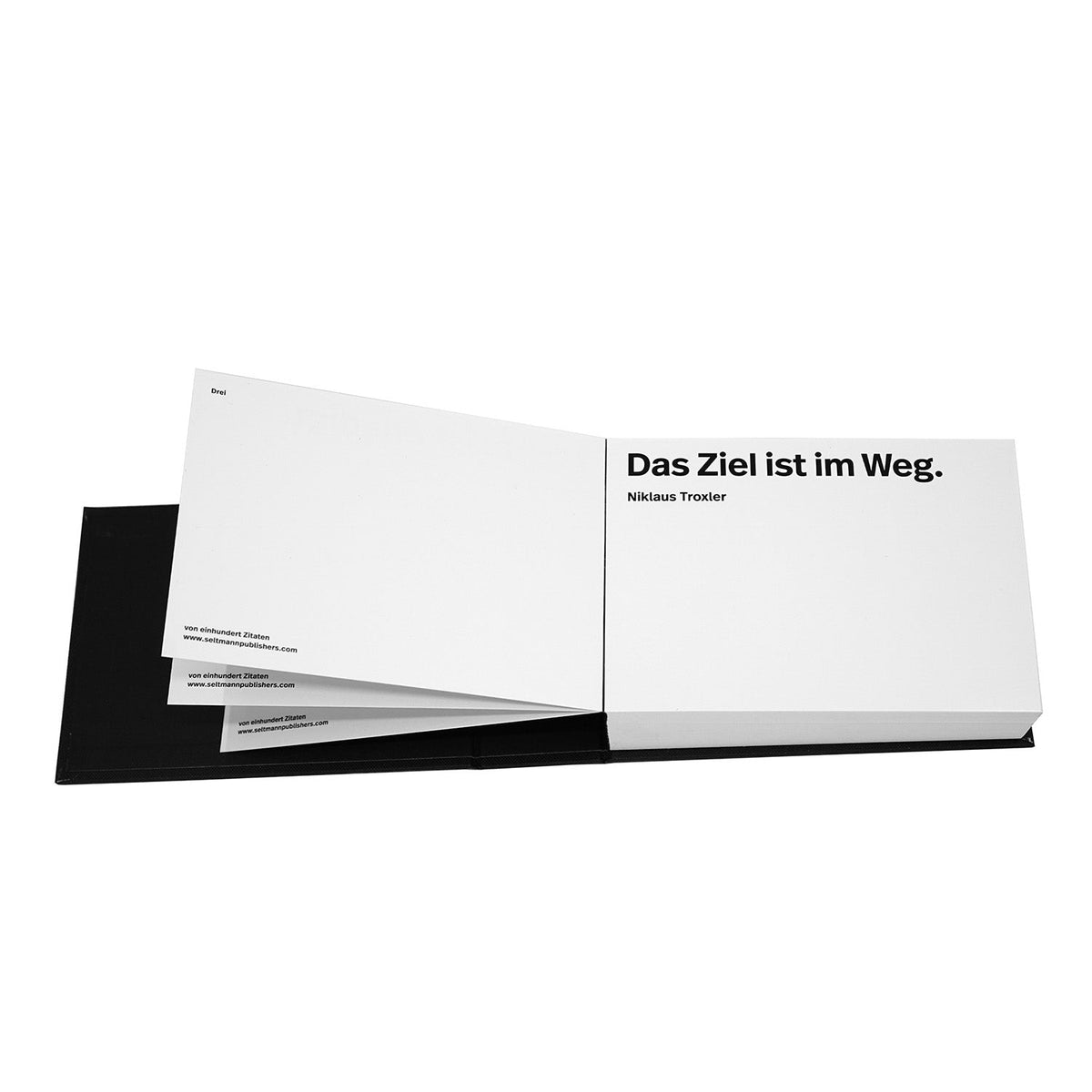 Aufgeschlagenes Buch mit dem Zitat "Das Ziel ist im Weg" von Niklaus Troxler auf schwarzem Untergrund vor weißem Hintergrund.