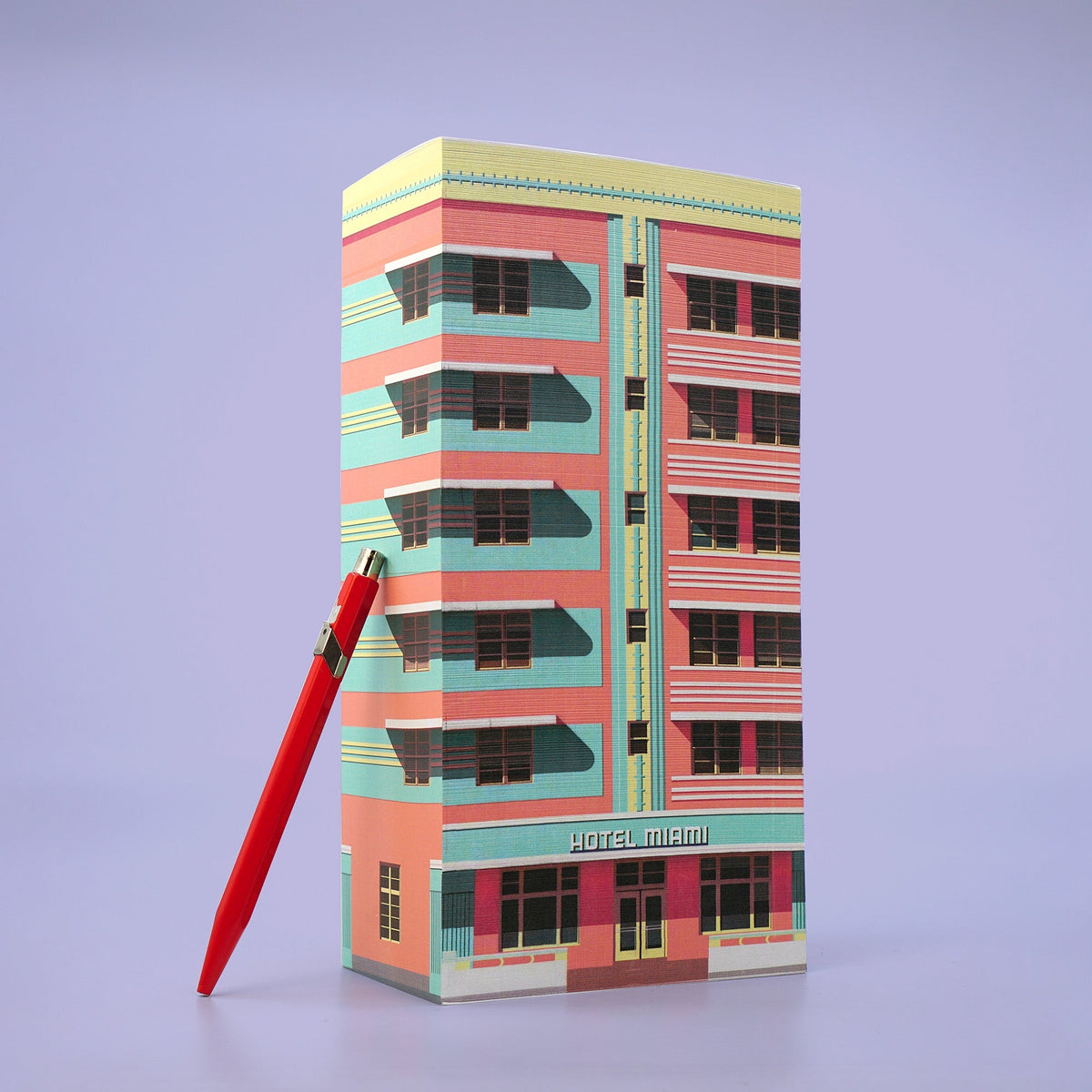 Hoher Papierblock mit Hotel-Motiv in Rosa und Türkis sowie rotem Stift davor.