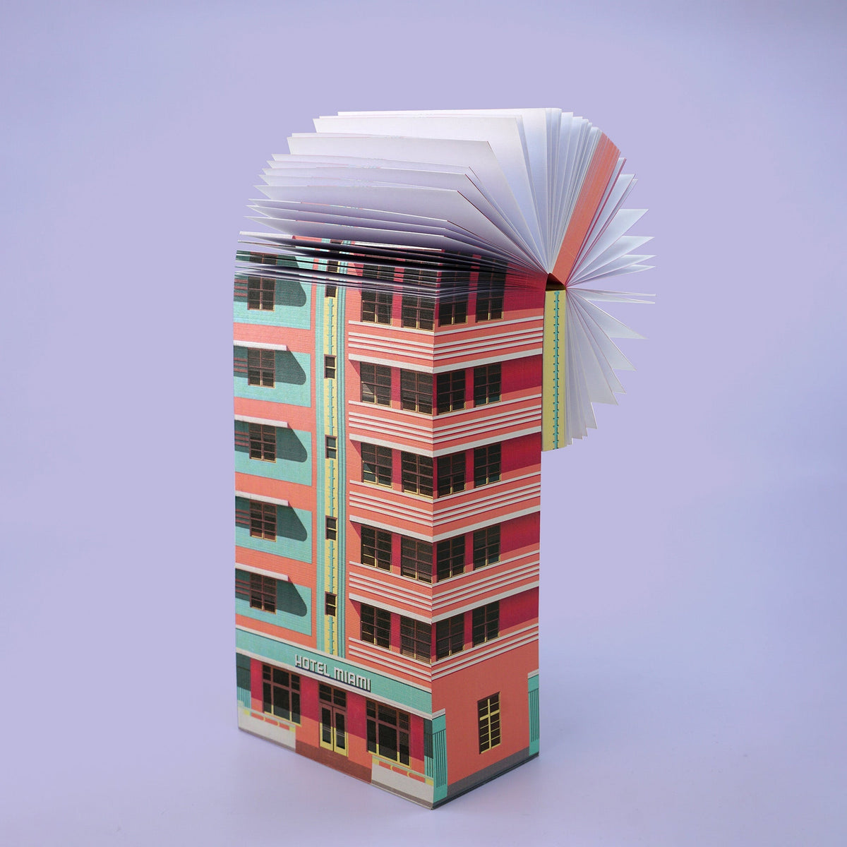 Aufgeschlagenes Buch mit gefalteten Seiten, die ein rosa-türkises Hochhaus mit der Aufschrift Hotel miami darstellen.