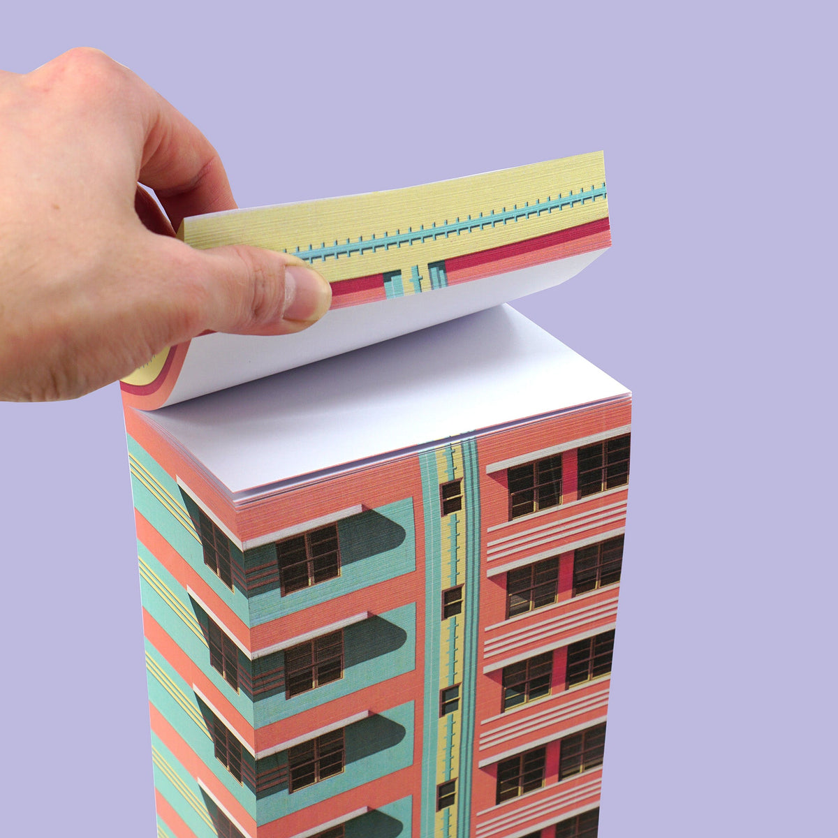 Eine Hand reißt ein Blatt von einem Papierblock mit Motiv eines rosa-türkisen Hochhauses vor lila Hintergrund.
