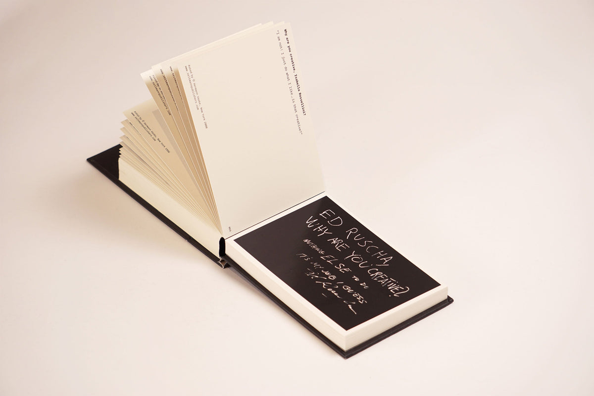Aufgeschlagenes Buch Why Are You Creative mit schwarzer Seite und weißem handschriftlichen Text von Ed Ruscha.
